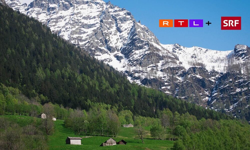 Eine idyllische Alpenlandschaft mit schneebedeckten Bergen, grünen Wiesen und verstreuten Steinhütten unter klarem blauem Himmel. | © SRF
