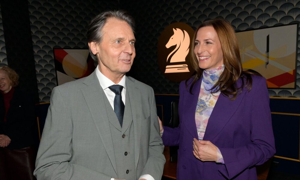 Ein grauhaariger Mann im grauen Anzug und eine braunhaarige Frau im lila Blazer lachen und unterhalten sich in einer stilvollen Lounge. | © RTL / Rolf Baumgartner