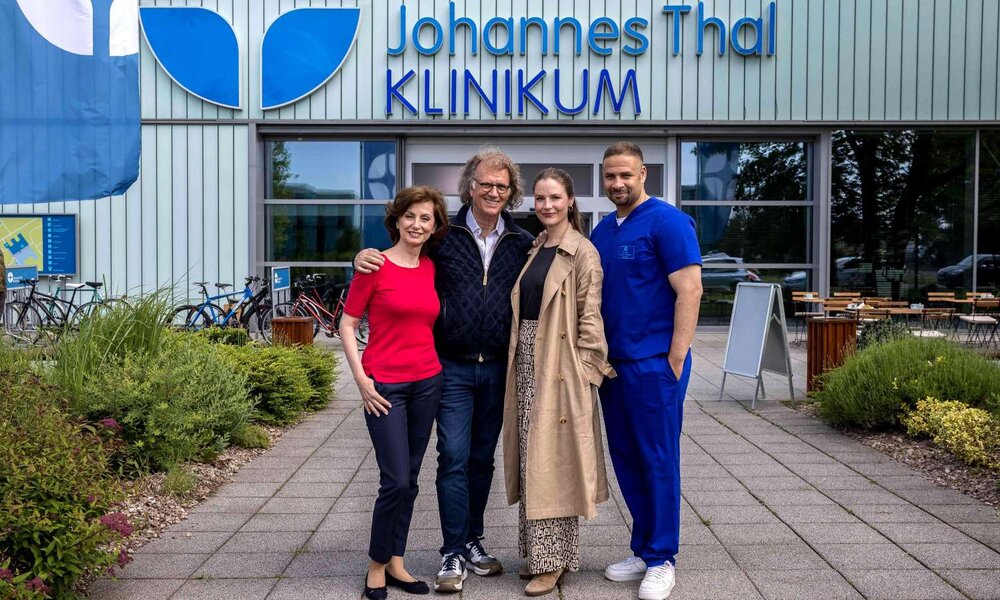 Eine Gruppe von zwei Frauen und zwei Männern posiert freundlich vor der Klinik, einer trägt medizinische Kleidung, die anderen Freizeit- und Businessmode. | © ARD/Michael Kremer