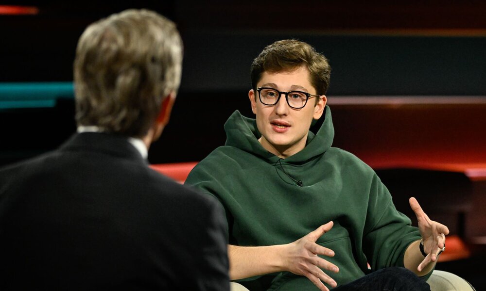 Ein junger Mann mit braunen Haaren, Brille und grünem Hoodie spricht gestikulierend in einer TV-Talkshow mit einem Moderator in Anzug. | © ZDF / Markus Hertrich