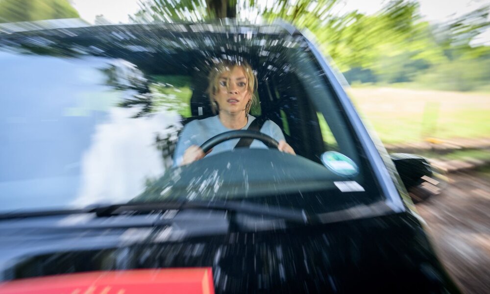 Eine junge Frau in blauem Oberteil steuert ein Auto mit panischem Gesichtsausdruck, die verwischte Landschaft deutet auf hohe Geschwindigkeit hin. | © ARD/WDR/Christof Arnold 