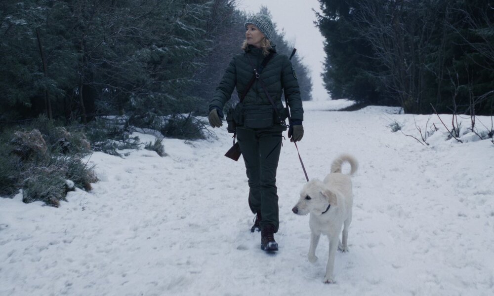 Eine blonde Frau in Winterkleidung und Strickmütze geht mit einem beigefarbenen Hund an der Leine durch eine verschneite Waldlandschaft. | © ZDF/Eckhard Jansen