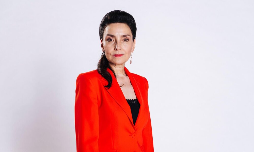 Eine Frau mit dunklen Haaren, roten Lippen und roten Ohrringen steht in einem leuchtend roten Blazer vor weißem Hintergrund. | © RTL / Julia Feldhagen