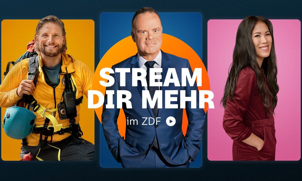 Ein Mann im blauen Anzug steht ernst vor einem blauen und orangefarbenen Hintergrund mit dem Schriftzug „STREAM DIR MEHR im ZDF“. | © ZDF/Sabine Finger/Tim Thiel/Jens Koch/ [M] serviceplan