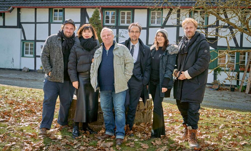 Eine Gruppe aus drei Männern und drei Frauen steht eng beieinander vor einem Fachwerkhaus, umgeben von fallendem Herbstlaub. | © WDR/Frank Dicks 