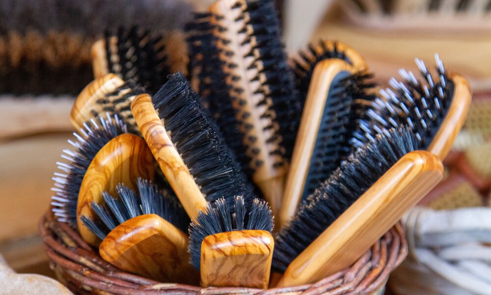 Ein brauner Strickkorb aus Holzfaser mit mehreren braunen Haarbürsten im Korb. Brauner Halter und schwarzer Bürstenkopf | © Adobe Stock/Dominik Ultes