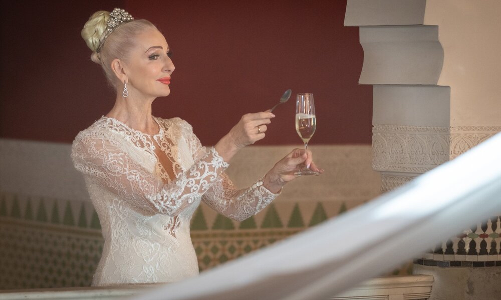 Juliane (Désirée Nick) steht im weißen Brautkleid mit einem Sektglas in der Hand in einem Raum. Sie schlägt mit einen Löffel an das Glas und lächelt. | © ZDF / Boris Laewen
