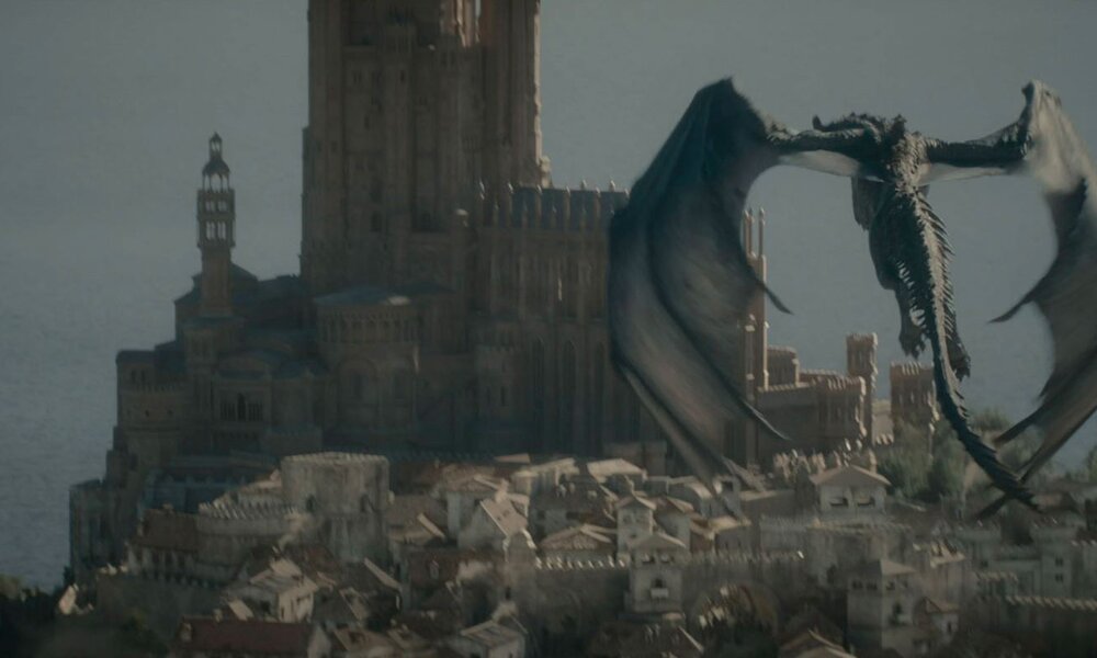 Ein schwarzer Drache mit ausgebreiteten Schwingen fliegt dramatisch über eine mittelalterliche Stadt mit gigantischer Burg. | ©  IMAGO / Landmark Media