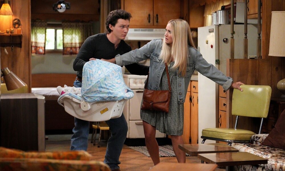 Ernster junger Mann mit Babyschale und blonde junge Frau in Jeansjacke wirken angespannt in einer rustikal eingerichteten Küche. | © 2024 Warner Bros. Entertainment Inc. All Rights Reserved. / Troy Harvey