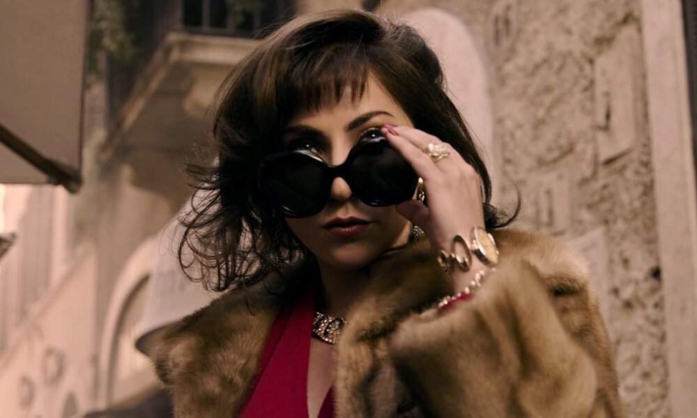 Junge Frau mit dunklem Bob und rotem Lippenstift hebt große schwarze Sonnenbrille, trägt Pelzmantel und goldenen Schmuck. | © RTL / 2021 Metro-Goldwyn-Mayer Pictures Inc.