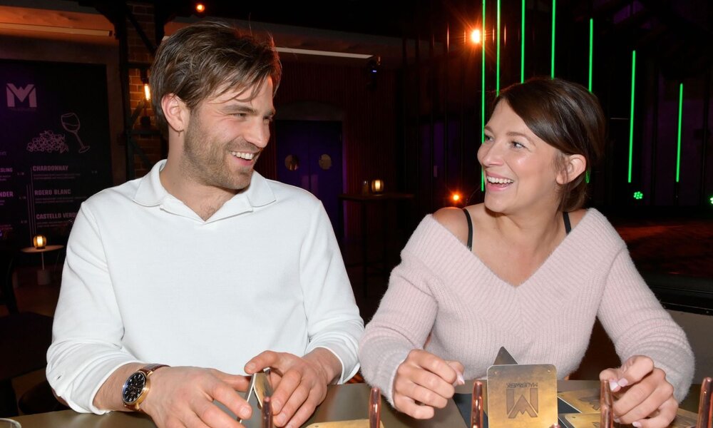 Junge Frau im rosafarbenen Pullover und junger Mann in weißem Shirt lachen sich an, während sie an einem Tisch in einer Bar sitzen. | © RTL / Rolf Baumgartner