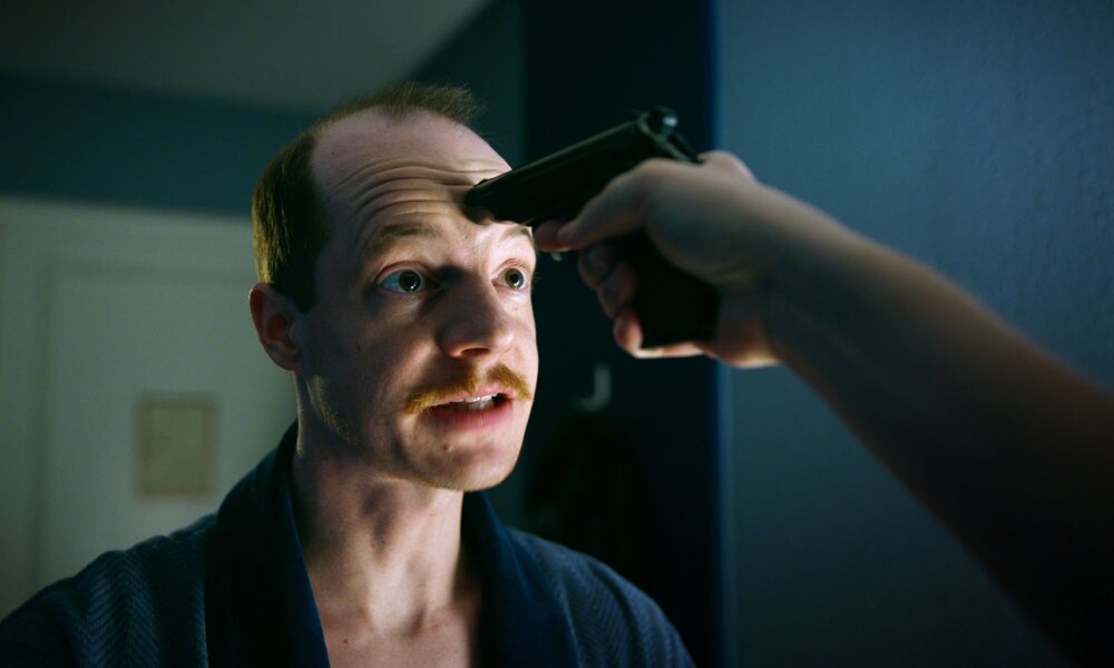 Nahaufnahme eines nervös dreinblickenden Mannes in Bedrängnis, dem eine Pistole direkt an die Stirn gedrückt wird. | © ARD Degeto Film/Superfilm Filmproduktions GmbH