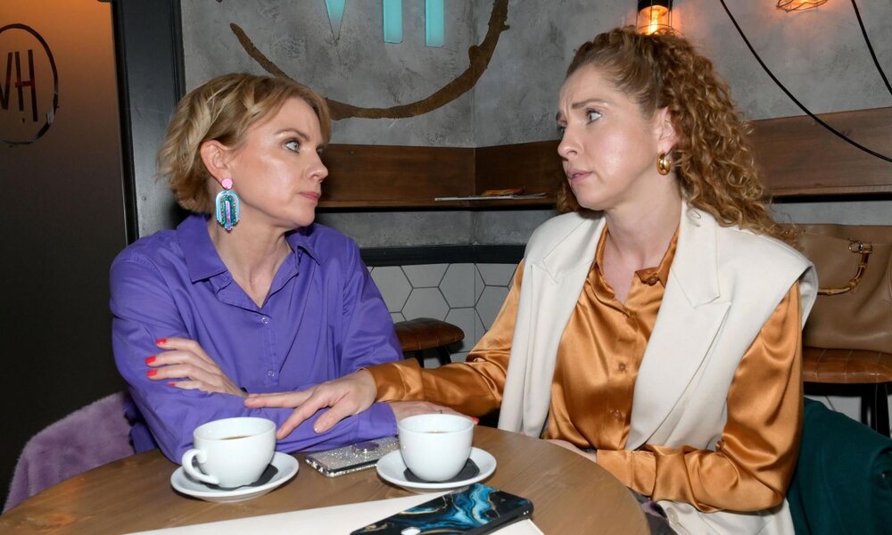 Eine Frau mit lila Bluse und bunter Ohrringe blickt nachdenklich auf eine andere mit Locken und goldener Bluse im Gespräch. | © RTL / Rolf Baumgartner