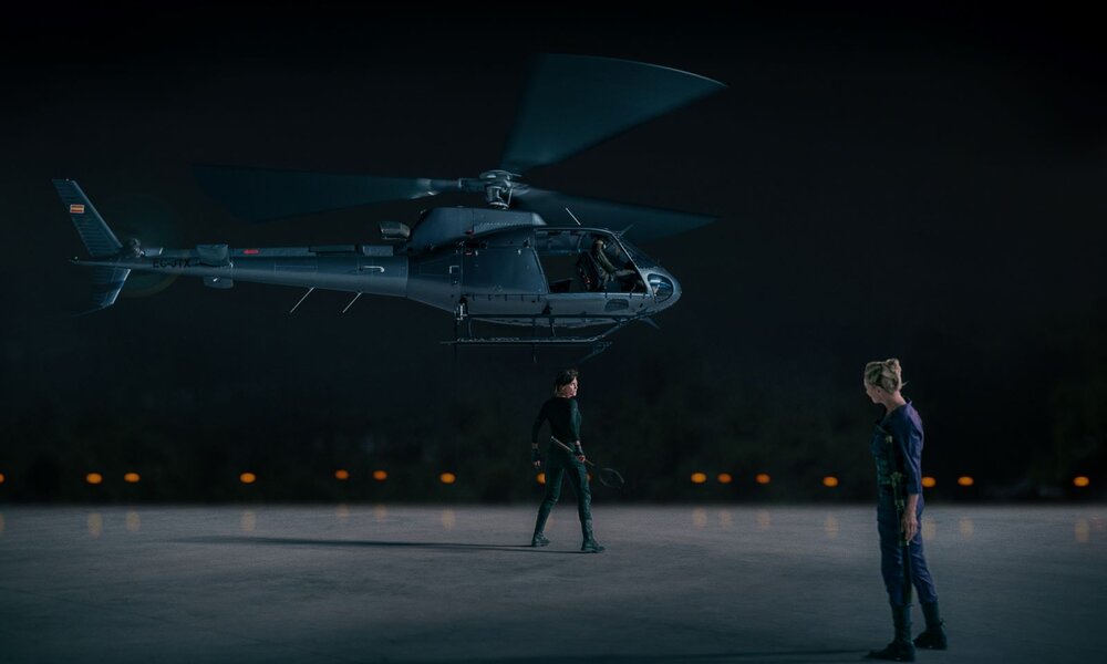 Zwei Personen in dunkler Einsatzkleidung stehen nachts unter einem schwebenden Helikopter auf leerem Betonplatz. | © Netflix