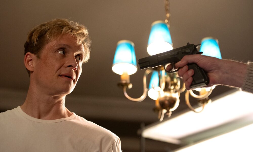 Angespannte Szene: Ein nervöser junger Mann ((Matthias Schweighöfer) schaut zur Seite, während ihm eine Waffe im warmen Licht entgegengestreckt wird. | © Netflix