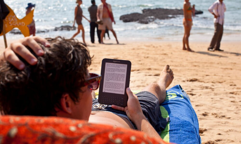 Mann am Strand mit E-Book-Reader | © Getty Images/EyesWideOpen