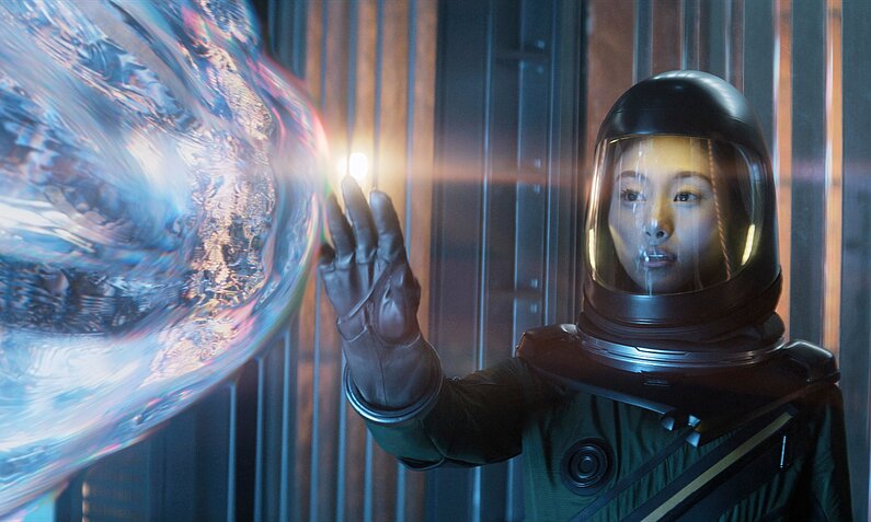 Shioli Kutsuna als Astronautin im Raumanzug bestaunt ein schimmerndes Objekt in einer Szene der Apple TV+ Serie "Infiltration" ("Invasion") | © Apple TV+