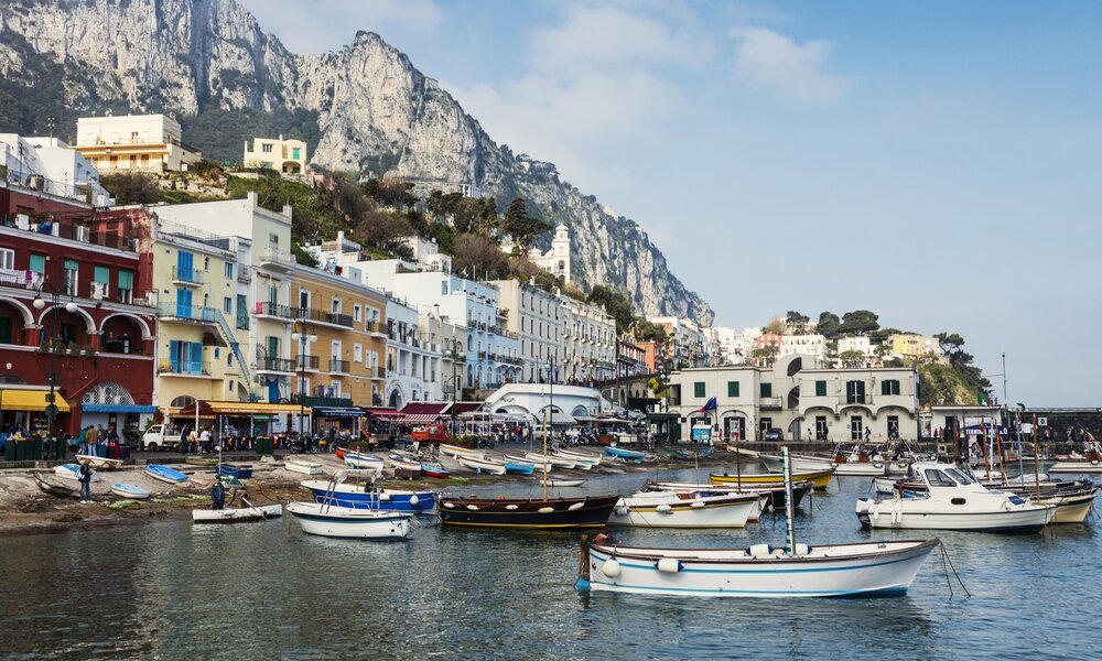 Ein Blick auf den Hafen von Capri mit vielen Fischerbooten und italienischen Häusern. Im Hintergrund sind große Felsen.  | ©  Getty Images / Henryk Sadura/Tetra Images