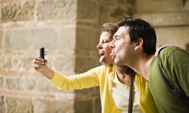 Touristenpärchen macht ein Selfie und zieht dabei Grimassen und streckt die Zunge raus  | ©  Getty Images / Zero Creatives