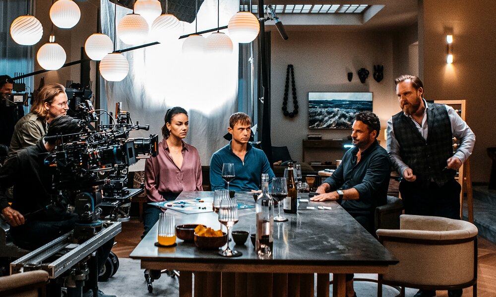Dennis Moyer und Janina Uhse beim Drehstart für den Netflix Film "Spieleabend", Die beiden Hauptdarstellerinnen sitzen in einem großen Wohnzimmer mit Edin Hasanovic an einem Tisch. Links von ihrer ist die Filmcrew mit Kameras, Mikrofonen und Co. zu sehen. | © Netflix/Sasha Ostrov