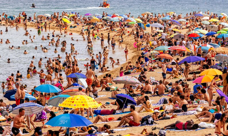 Überfüllter Sandstrand am Meer mit hunderten von Gästen und Sonnenschirmen  | ©  Getty Images / Alexander Spatari