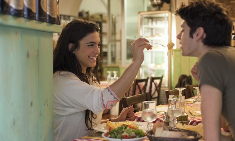 Pärchen isst in einem italienischen Restaurant. Die Frau reicht dem Mann eine Gabel mit Pasta an. | ©  Getty Images / Kathrin Ziegler