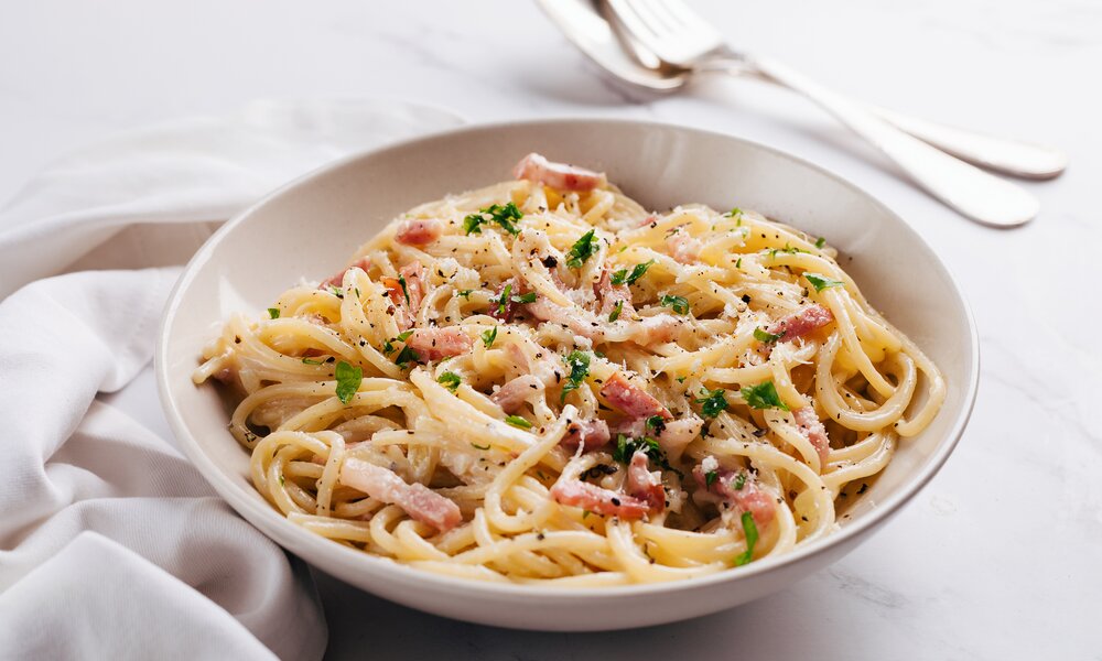 Ein Teller voller Spaghetti und Carbonana. Der Teller steht auf einer weißen Tischdecke und daneben liegt Besteck.  | © Getty Images / Cris Cantón