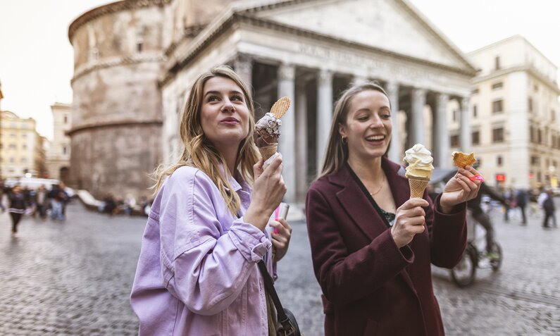 Zwei junge Frauen essen in einer italienischen Kulisse ein Eis | ©  Getty Images / piola666