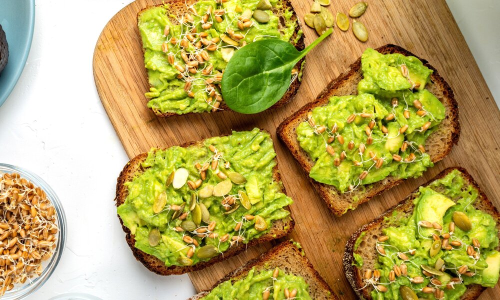 Auf einem brett liegen einige Scheiben Brot belegt mit Erbsenpüree und Sprossen. Naben liegen lose einige Kürbiskerne und eine Schale mit Sprossen darin | © Getty Images / RoNeDya