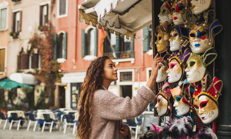 Frau steht an einem Souvenir-Stand und schaut sich venezianische Masken an. | ©  Getty Images / Oleg Breslavtsev