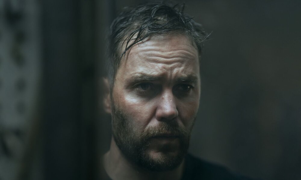 Taylor Kitsch sieht sich selbst im Spiegel an. Seine Haare sind verschwitzt und zauselig und er wirkt extrem blass. | © Netflix