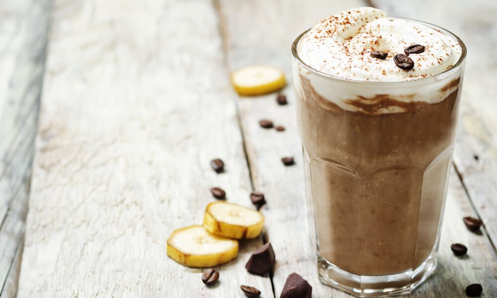 Ein Glas gefüllt mit einer Kaffee-Creme. Daneben lieben Bananenscheiben. Das Glas steht auf einem alten Holztisch | © Getty Images / nata_vkusidey
