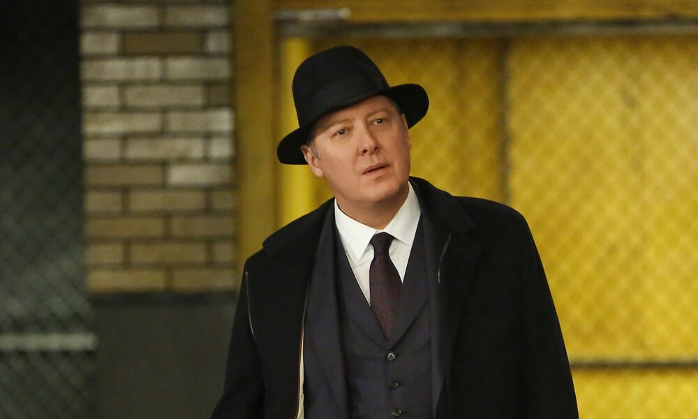 James Spader als Raymond "Red" Reddington in einer Szene  der Serie "The Blacklist". Er trägt seinen Markenzeichen-Hut, einen Mantel und steht in einem Keller/einer Garage vor einem Aufzug. | © Getty Images /Will Hart/NBCU Photo Bank/NBCUniversal