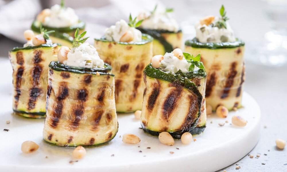 Gegrillte Zucchini-Röllchen befüllt mit Fetakäse, drapiert auf einem weißen Teller, in Nahaufnahme. | © Getty Images / Azurita