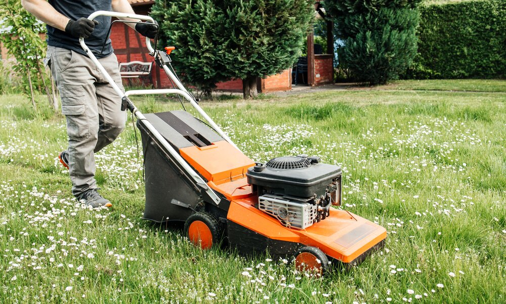 Mann mäht mit einem orangenen Rasenmäher eine Wiese | ©  Getty Images / Elena Medoks