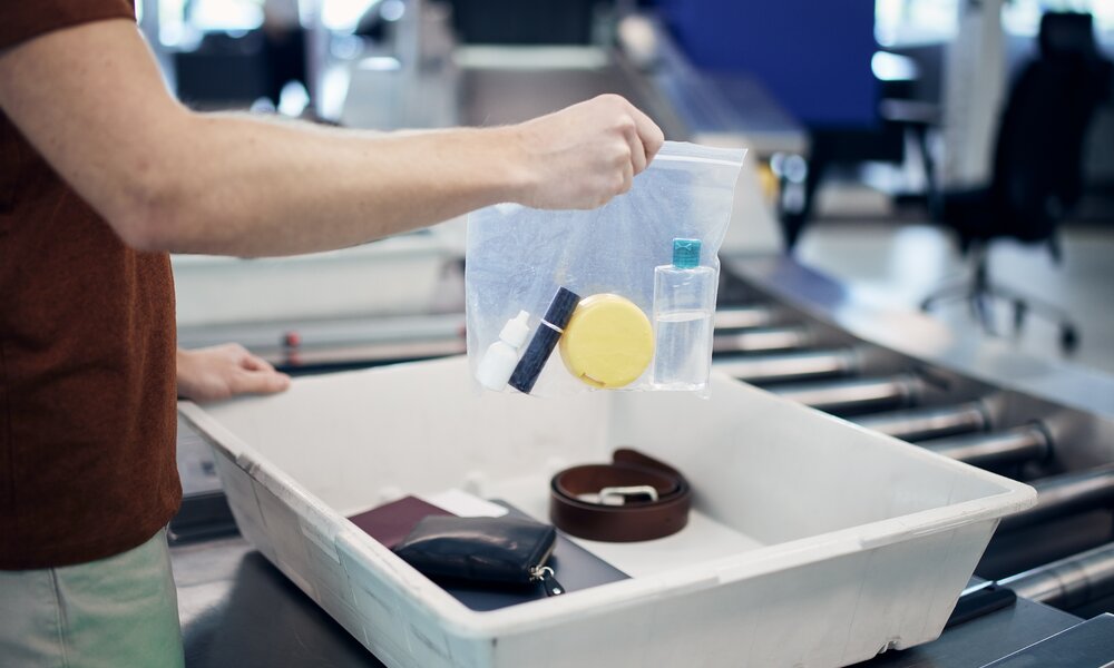 Mann packt seine abgepackten Flüssigkeiten in einer Tüte in die Box der Sicherheitskontrolle | ©  Getty Images / Chalabala