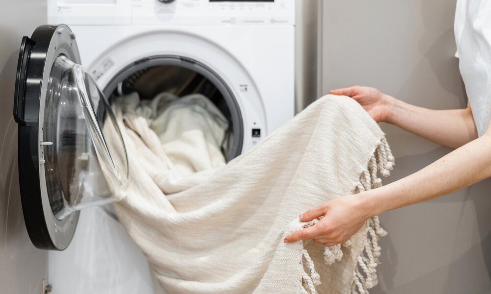 Frau beim Entladen von Wäsche aus weißer Waschmaschine | ©  Getty Images / brizmaker