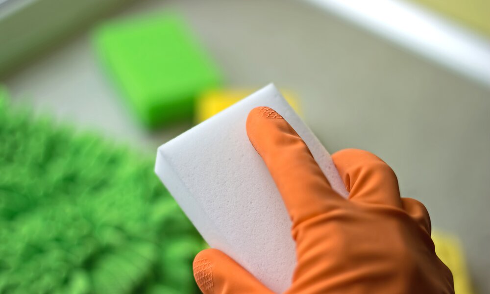 Hand mit orangenem Putzhandschuh hält einen Schmutzradierer | ©  Getty Images / Irina Vodneva