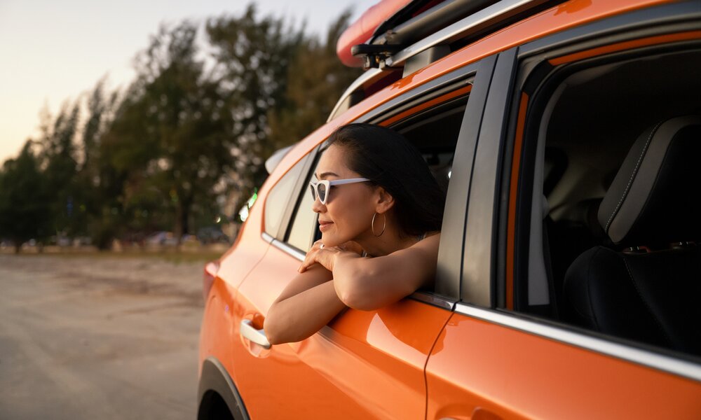 Frau mit Sonnenbrille lehnt sich aus dem Fenster eines fahrenden Autos | ©  Getty Images / Patchareeporn Sakoolchai