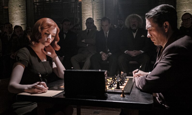 Anya Taylor-Joy als Beth Harmon und Marcin Dotocinski als Vasily Borgov der Netflix-Serie "Das Damengambit". Die beiden sitzen sich in einem dunklen Raum gegenüber und spielen Schach. | © Netflix/Phil Bray