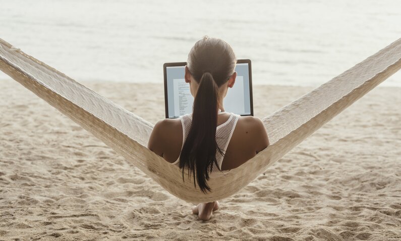Frau sitzt in Hängematte am Strand, auf ihrem Schoß ein Laptop | ©  Getty Images / Cavan Images