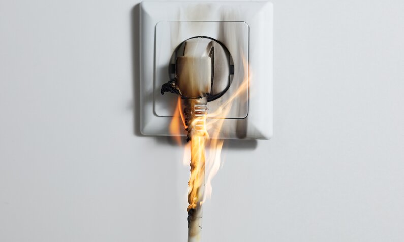 Ein brennender Stecker in der Steckdose | ©  Getty Images / AndreyPopov