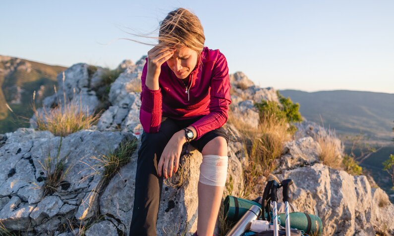 Frau sitzt verletzt auf einem Felsen | ©  Getty Images / FluxFactory