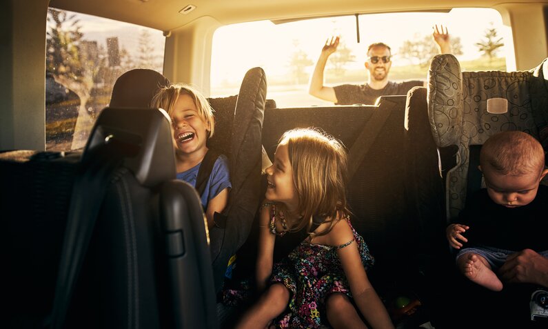 Kinder sitzen lachend auf der Rückbank vom Auto  | ©  Getty Images / pixdeluxe