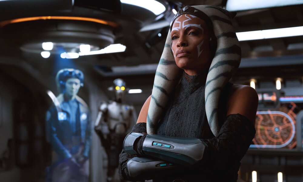 Rosario Dawson als Ex-Jedi Ahsoka in der gleichnamigen "Star Wars"-Serie an Bord eines Raumschiffes - im Hintergrund sind ein Wesen in Blau und ein Droide zu sehen. | © Disney+/Lucasfilm
