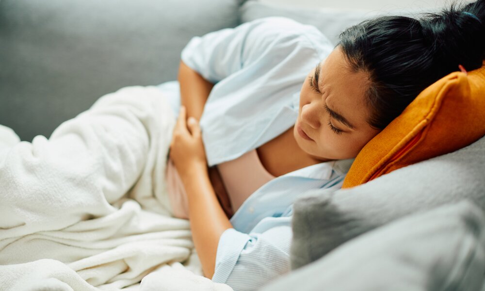  Frau liegt auf Sofa und hält sich den Bauch  | ©  Getty Images / Drazen Zigic