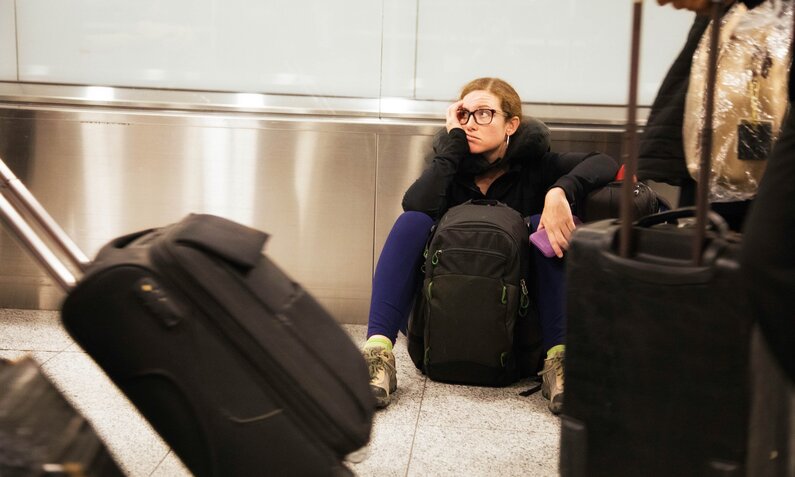 Frau sitzt erschöpft am Gepäckband | ©  Getty Images / NicolasMcComber