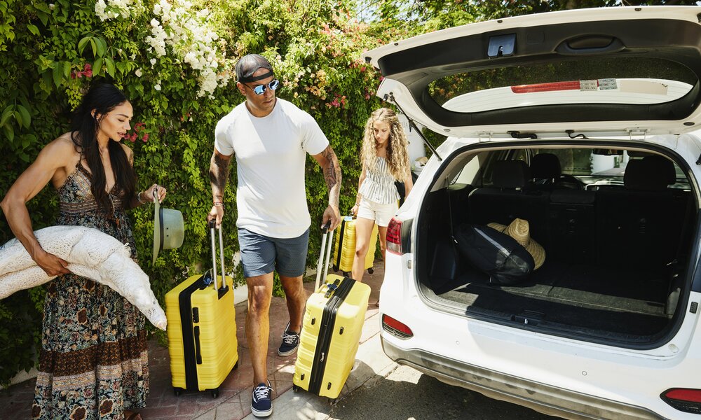 Leute tragen ihr Gepäck zum offenen Kofferraum eines Autos | ©  Getty Images / Thomas Barwick