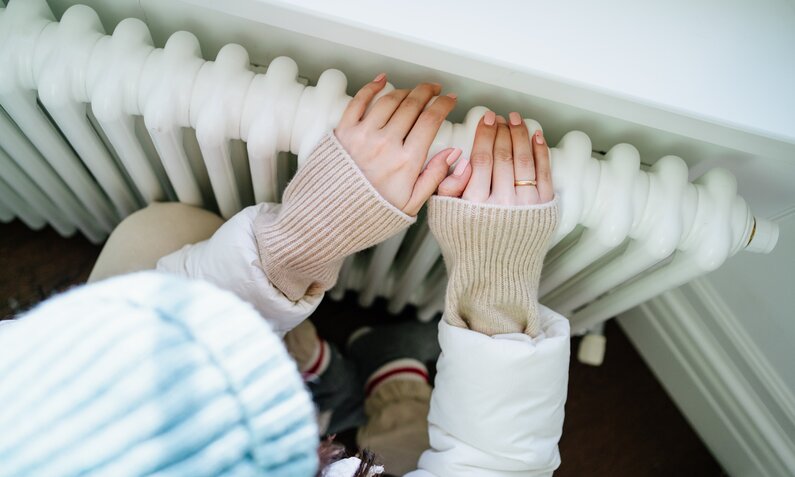 Frau wärmt sich die Hände an der Heizung  | ©  Getty Images / Tatiana Meteleva