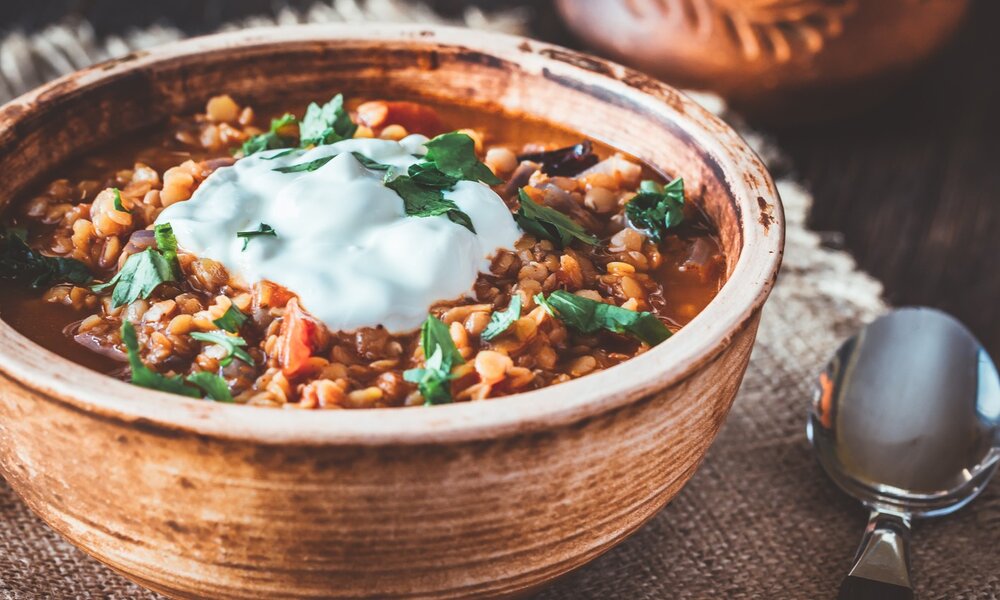 Eine Schüssel gefüllt mit Linsensuppe, bestückt mit Schmand-Topping und frischen Kräutern.  | © Getty Images / AlexPro9500